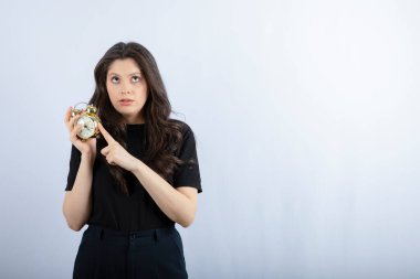 Siyah elbiseli esmer kızın portresi beyaz arka planda saati tutuyor. Yüksek kalite fotoğraf