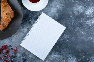 Bir fincan kruvasanla çay ve taş masaya yerleştirilmiş bir defter. Yüksek kalite fotoğraf