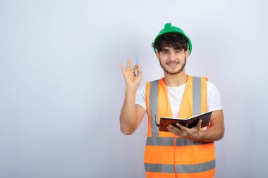 Beyaz duvarın üzerinde duran yeşil şapkalı yakışıklı erkek mühendis. Yüksek kalite fotoğraf