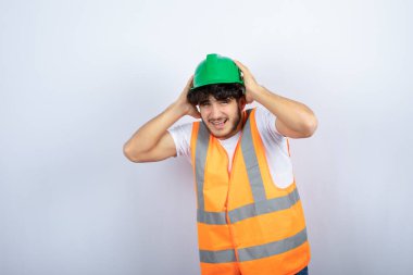 Kulaklarını tutan yeşil şapkalı genç bir inşaat işçisi. Yüksek kalite fotoğraf