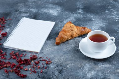 Taze ve lezzetli kruvasan, bir fincan sıcak çay ve defter. Yüksek kalite fotoğraf