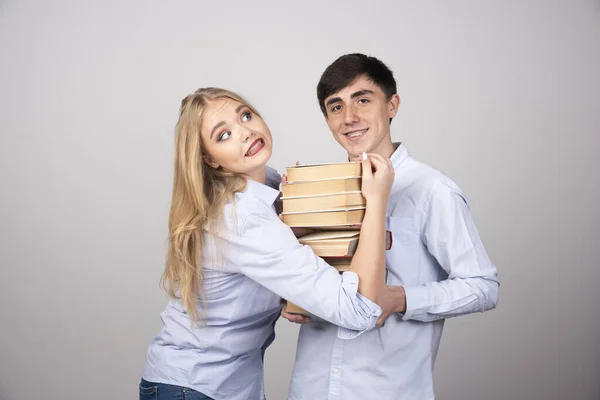 若い素敵なカップルは灰色の背景に本の束を保持します 高品質の写真 — ストック写真