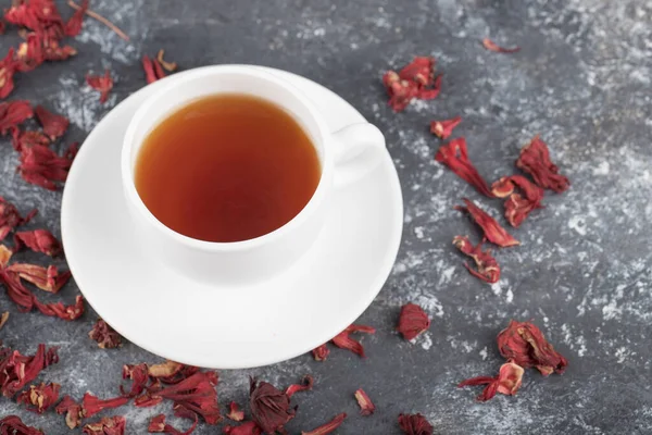 White cup of hot black tea with dried flower buds placed on a dark grey background . High quality photo