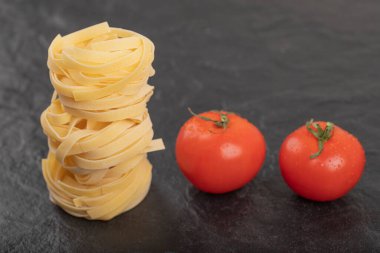 Siyah yüzeyde taze domatesli çiğ tagliatelle yuvaları. Yüksek kalite fotoğraf