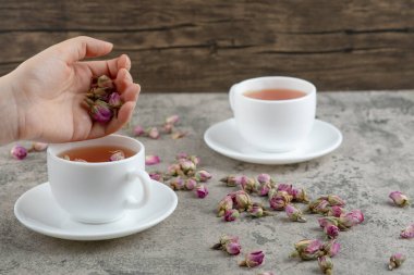 Kadın eli, mermer arka plandaki çay fincanına kurumuş çiçekler ekler. Yüksek kalite fotoğraf