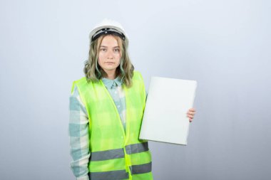 Güzel bayan mühendisin beyaz duvarın üzerinde boş tuval tutarken çekilmiş fotoğrafı. Yüksek kalite fotoğraf