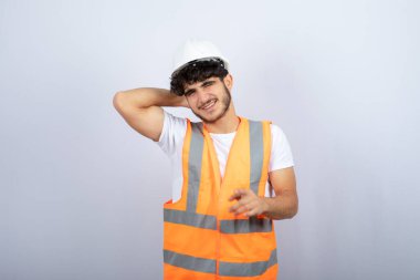 Beyaz kasklı yakışıklı genç adam beyaz duvarın üzerinde kameraya poz veriyor. Yüksek kalite fotoğraf