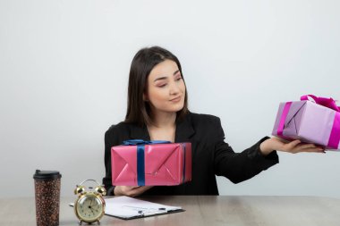 İş yerinde elinde hediyelerle oturan iş kadınının portresi.