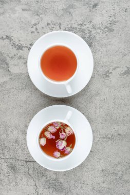 Beyaz bir fincan, mermer arka planda solmuş gül çiçekleri olan lezzetli bir çay. Yüksek kalite fotoğraf