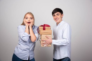 Gülümseyen adam gri arka planda hediyelerle kız arkadaşına sürpriz yapıyor. Yüksek kalite fotoğraf