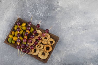 Kurumuş elma halkaları, kumkatlar ve mermer zemin üzerinde kırmızı üzümlerle dolu ahşap bir tabak. Yüksek kalite fotoğraf