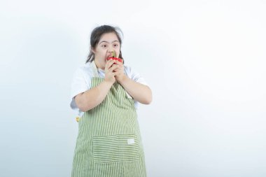 Kareli önlüğün içinde duran ve kırmızı dolma biber yiyen genç ve güzel bir kız. Yüksek kalite fotoğraf