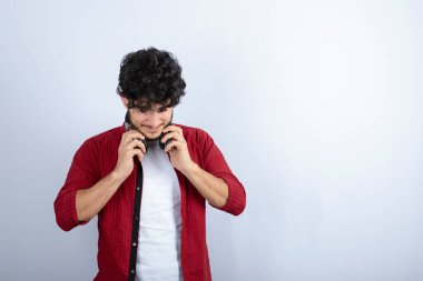 Kulaklıklı genç bir adamın beyaz arka planda dezavantajlara baktığı bir görüntü. Yüksek kalite fotoğraf