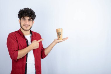 Sıradan kıyafetli genç adamın resmi beyaz arka plandaki bir fincan kahveyi işaret ediyor. Yüksek kalite fotoğraf