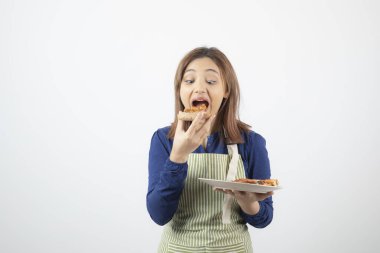 Önlüklü, pizza yiyen genç ve güzel bir kadının fotoğrafı.