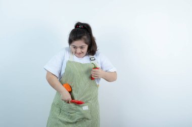 Kareli önlüğün içinde duran ve cebine sebze koyan genç ve güzel bir kız. Yüksek kalite fotoğraf