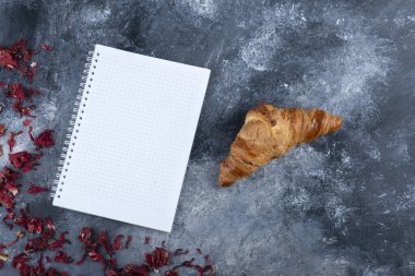 Taze ve lezzetli kruvasan ve açık bir defter. Yüksek kalite fotoğraf