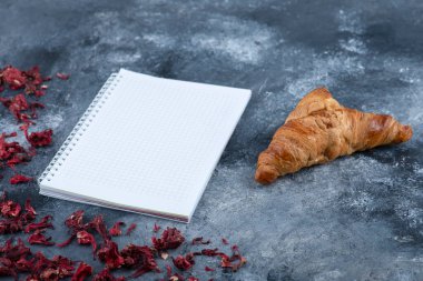 Mermer bir masaya yerleştirilmiş boş bir defter ile sade kruvasan. Yüksek kalite fotoğraf