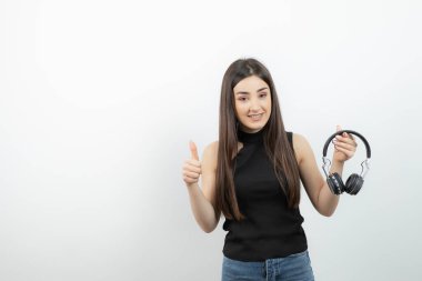 Siyah tişörtlü, kablosuz kulaklıklı, baş parmağını kaldıran sevimli bir kadın. Yüksek kalite fotoğraf