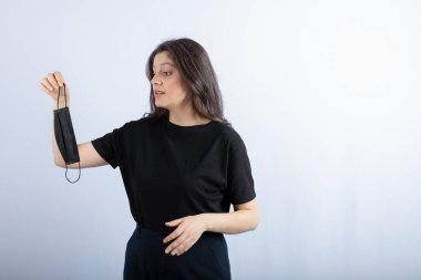 Güzel esmer kız beyaz duvarın üzerinden tıbbi maskeye bakıyor. Yüksek kalite fotoğraf