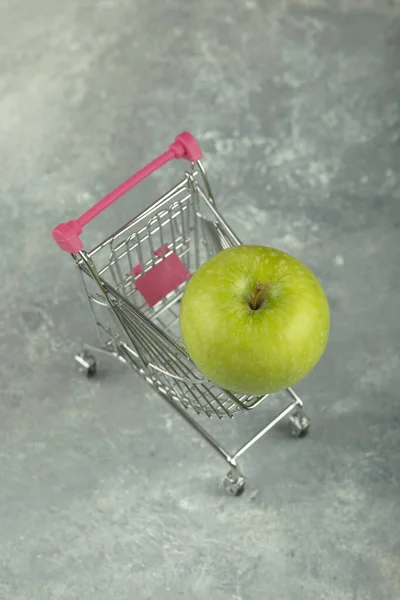 大理石の背景にショッピングカートと緑のジューシーなシングルアップル 高品質の写真 — ストック写真