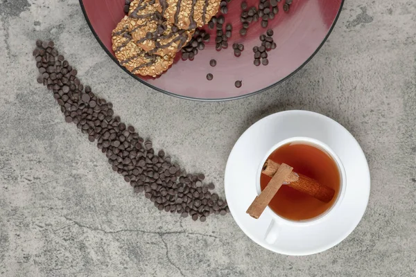 Kırmızı tabağa çikolata damlaları serpiştirilmiş lezzetli kurabiyeler ve bir fincan çay. Yüksek kalite fotoğraf