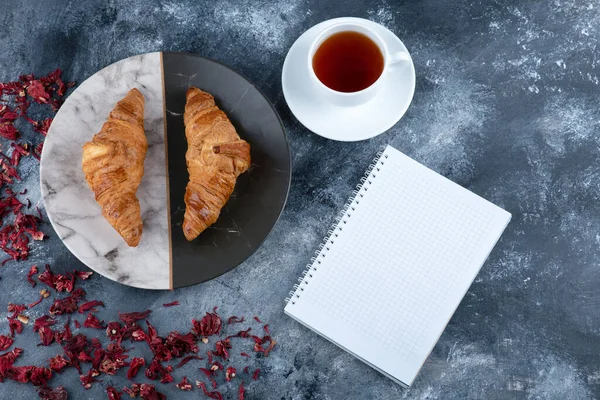 Bir fincan kruvasanla çay ve taş masaya yerleştirilmiş bir defter. Yüksek kalite fotoğraf
