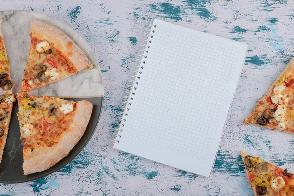 Mermer zemin üzerinde defter olan sıcak pizza dilimleri. Yüksek kalite fotoğraf