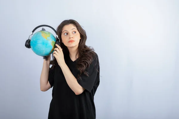 若いブルネットの女性が彼女の手の中に地球とヘッドフォンで立っている 高品質の写真 — ストック写真