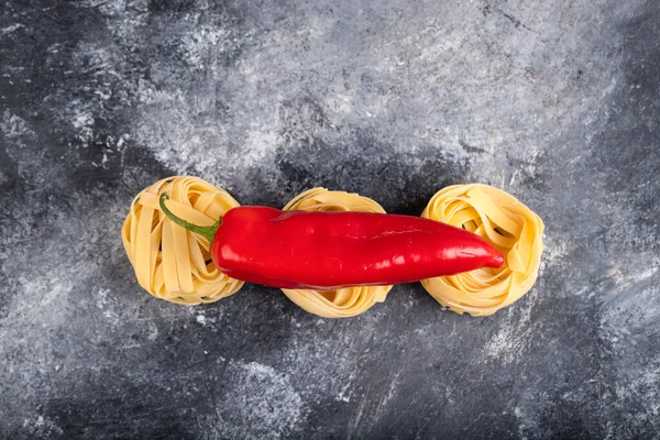 Mermer yüzeyinde kırmızı biberli çiğ makarna yuvaları. Yüksek kalite fotoğraf