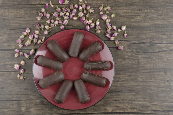 Çikolatalı kremayla dolu kırmızı bir tabak süt kremalı ve ahşap bir masada kurumuş güller. Yüksek kalite fotoğraf