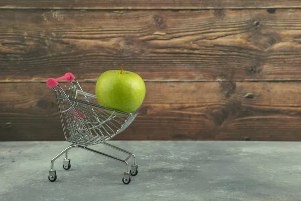 大理石の背景にショッピングカートと緑のジューシーなシングルアップル 高品質の写真 — ストック写真