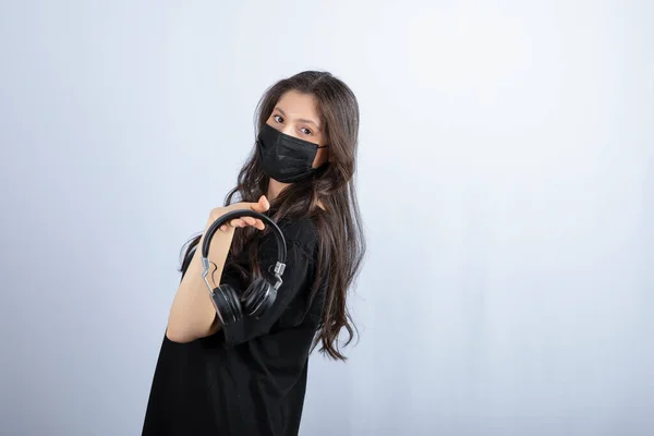 Brunette woman with long hair in medical mask holding headphones . High quality photo