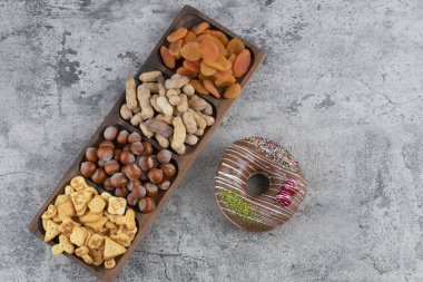 Tahta tabak dolusu fındık, kraker ve mermer yüzeyde çikolatalı çörekle kurutulmuş kayısı. Yüksek kalite fotoğraf