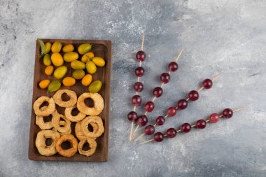 Kurumuş elma halkaları, kumkatlar ve mermer zemin üzerinde kırmızı üzümlerle dolu ahşap bir tabak. Yüksek kalite fotoğraf