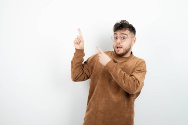 Beyaz duvarın üzerinde duran ve işaret eden genç yakışıklı adamın fotoğrafı. Yüksek kalite fotoğraf