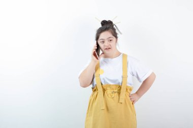 Genç ve güzel kız model ayakta duruyor ve beyaz duvara karşı cep telefonuyla konuşuyor. Yüksek kalite fotoğraf