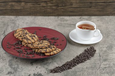 Kırmızı tabağa çikolata damlaları serpiştirilmiş lezzetli kurabiyeler ve bir fincan çay. Yüksek kalite fotoğraf