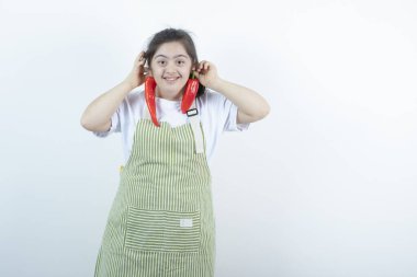 Kareli önlüğün içinde duran ve elinde iki kırmızı acı biber tutan genç ve güzel bir kız. Yüksek kalite fotoğraf