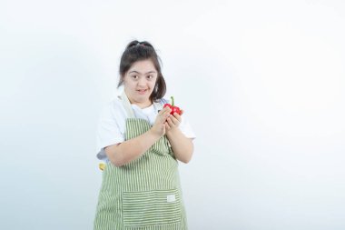 Kareli önlüğün içinde duran ve elinde kırmızı dolma biber tutan genç ve güzel bir kız. Yüksek kalite fotoğraf