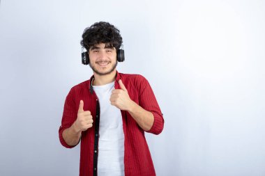 Kulaklıklı yakışıklı bir gencin beyaz duvarda şarkı dinlediği bir görüntü. Yüksek kalite fotoğraf