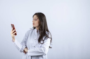 Genç doktorun beyaz arka planda cep telefonuyla bir şeyler okuduğu fotoğraf. Yüksek kalite fotoğraf