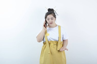 Genç ve güzel kız model ayakta duruyor ve beyaz duvara karşı cep telefonuyla konuşuyor. Yüksek kalite fotoğraf