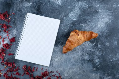 Mermer bir masaya yerleştirilmiş boş bir defter ile sade kruvasan. Yüksek kalite fotoğraf