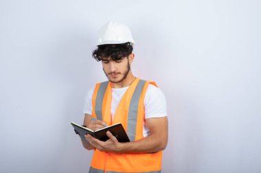 Beyaz duvarın üzerinde deftere yazılı, kasketli yakışıklı erkek mühendis. Yüksek kalite fotoğraf