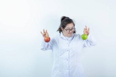 Doktor üniformalı genç bir kız elinde yeşil ve kırmızı elma meyveleri tutuyor. Yüksek kalite fotoğraf