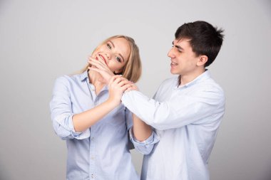 Gri duvara yaslanmış neşeli erkek arkadaşının elini ısıran bir kadın. Yüksek kalite fotoğraf