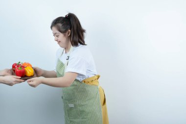 Önlüklü genç ve güzel bir kız taze sebzelerle tahta tahtayla ayakta duruyor. Yüksek kalite fotoğraf