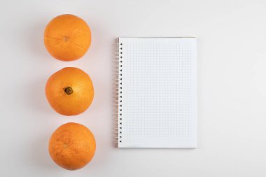 Beyaz defterin etrafında üç tane taze portakal. Yüksek kalite fotoğraf