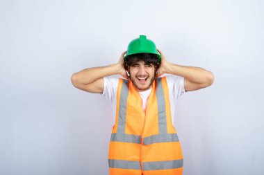 Kulaklarını tutan yeşil şapkalı genç bir inşaat işçisi. Yüksek kalite fotoğraf